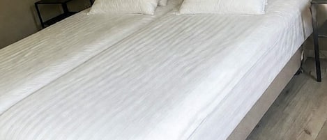 A single bed with white bedding in a room with a wooden floor and a nightstand with a lamp.