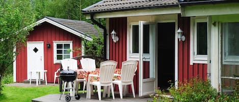A red building with a porch, outdoor seating, and a grill.