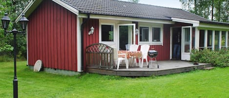 A red wooden building with a porch, a table with chairs, and a grill.