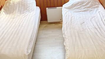 Una habitación con dos camas individuales, paneles de madera en las paredes y un radiador entre las camas.