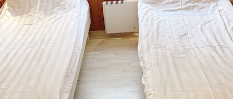 A room with two single beds, wooden paneling on the walls, and a radiator between the beds.