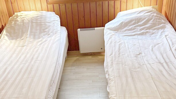 Una habitación con dos camas, paneles de madera en las paredes y un radiador entre ellas.