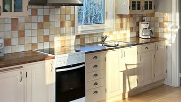 Una cocina con estufa a gas, horno, lavaplatos y ventana con vistas a árboles.