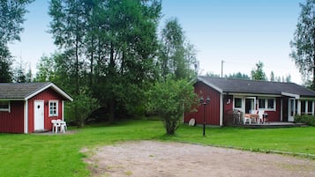 Two red buildings with a grassy area in between, a small tree, and a gravel path.
