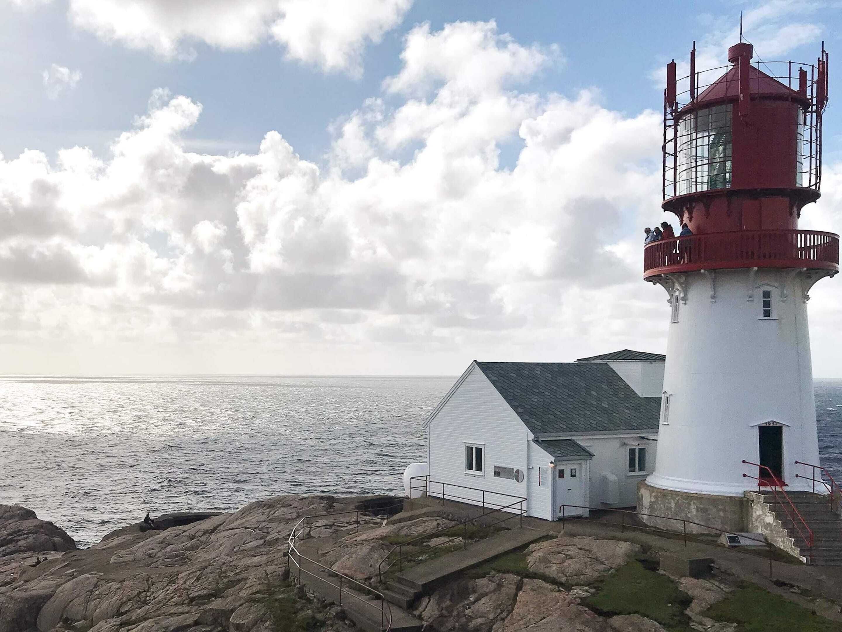 Ein Leuchtturm mit weißem Unterteil und roter Spitze, gelegen auf felsigem Gelände mit Blick aufs Meer.