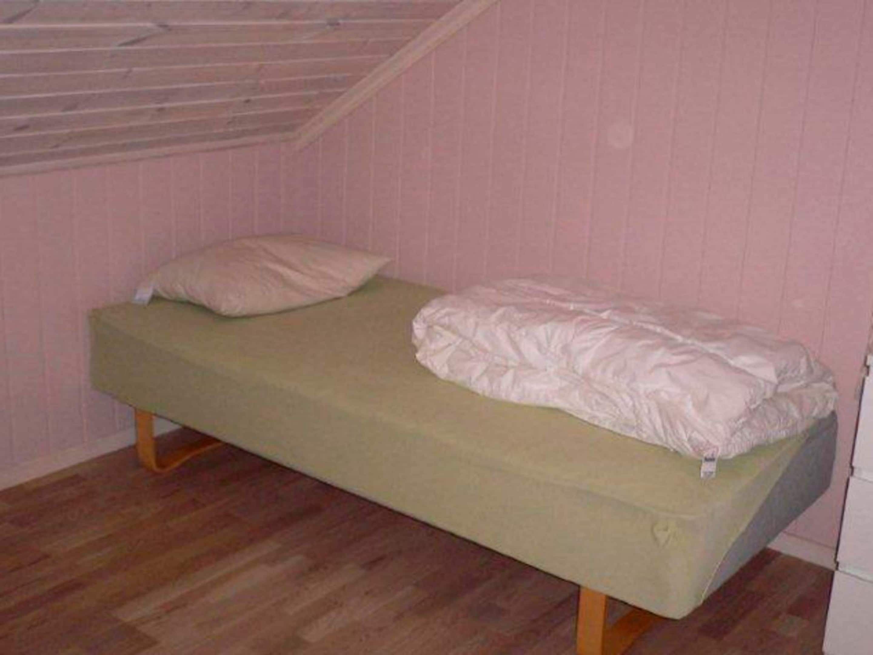 Una cama individual con colchón verde y ropa de cama blanca en una habitación con paredes rosas y suelo de madera.