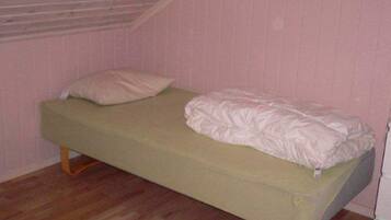 Una cama individual con colchón verde y ropa de cama blanca en una habitación con paredes rosas y suelo de madera.