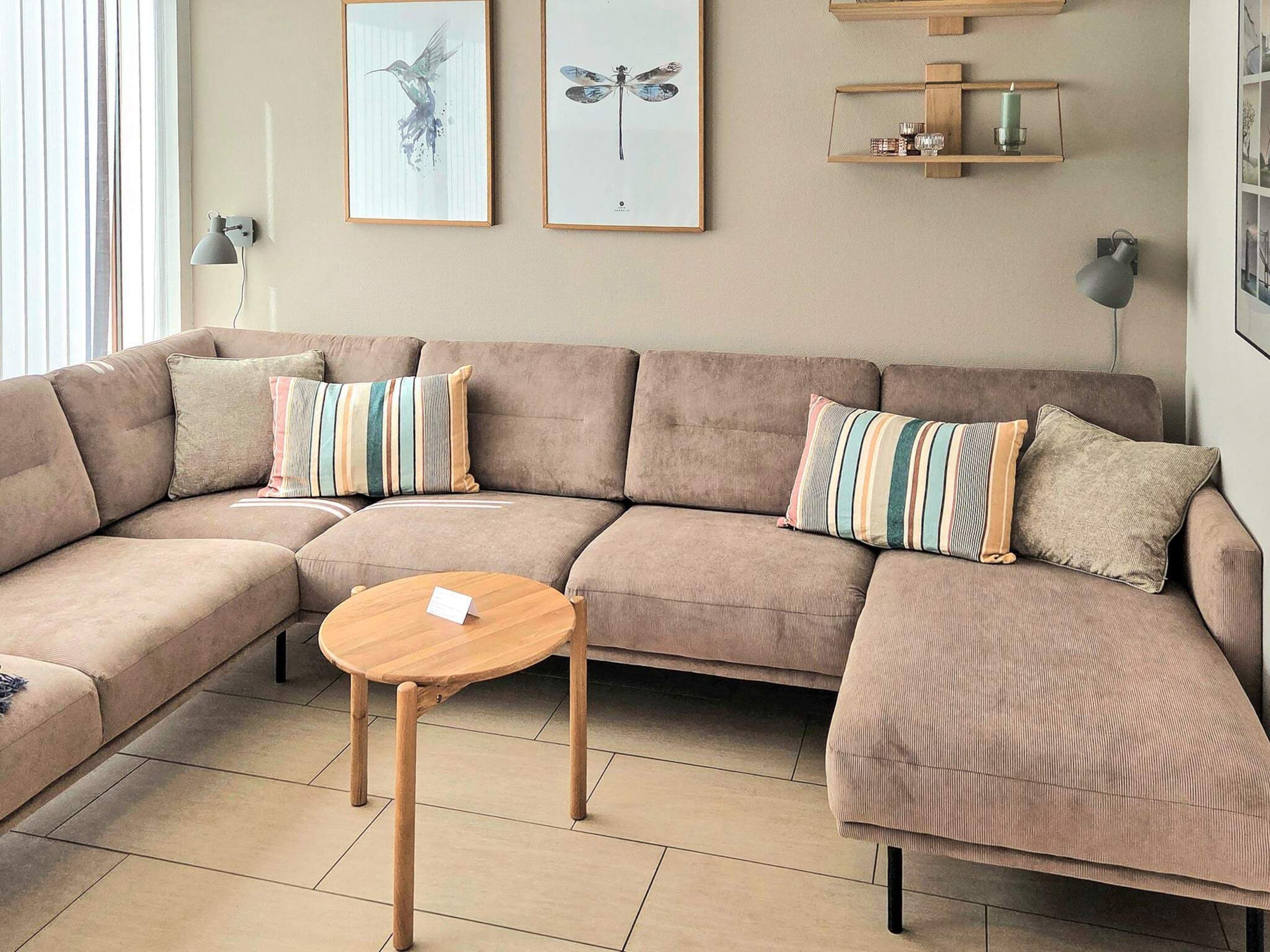 A modern living room with a sectional sofa, a round wooden coffee table, and two wall-mounted shelves with decorative items.