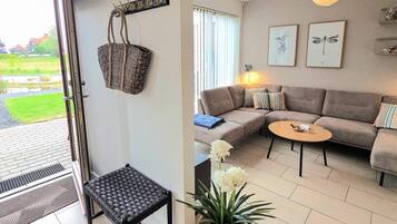 En stue med sofa, et lille bord, en fletkurv, en bænk og en potteplante.