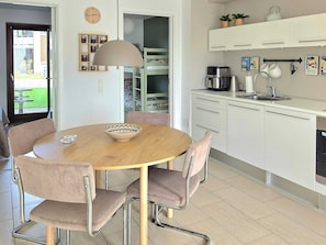 A modern kitchen with white cabinets, a round dining table with chairs, a hanging light fixture, and a view of a balcony. - 4 Star Holiday Home in Bogense (Bogense)