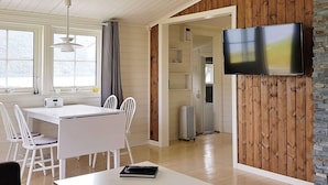 Eine moderne Küche mit weißen Schränken, einem Esstisch mit Stühlen, einem eingebauten Backofen und einem großen Flachbildfernseher an der Wand.
