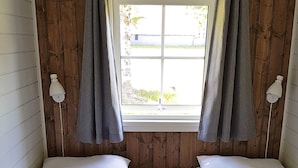 Ein Zimmer mit zwei Betten, Holzwänden, einem Fenster mit Vorhängen und Wandleuchten.