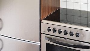 Eine Küche mit Edelstahl-Kühlschrank und -herd, einem Holzschrank und einer gefliesten Spritzschutzwand.