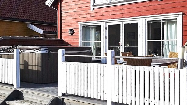 Een rode houten woning met een witte omheining, een terras en tuinmeubilair.