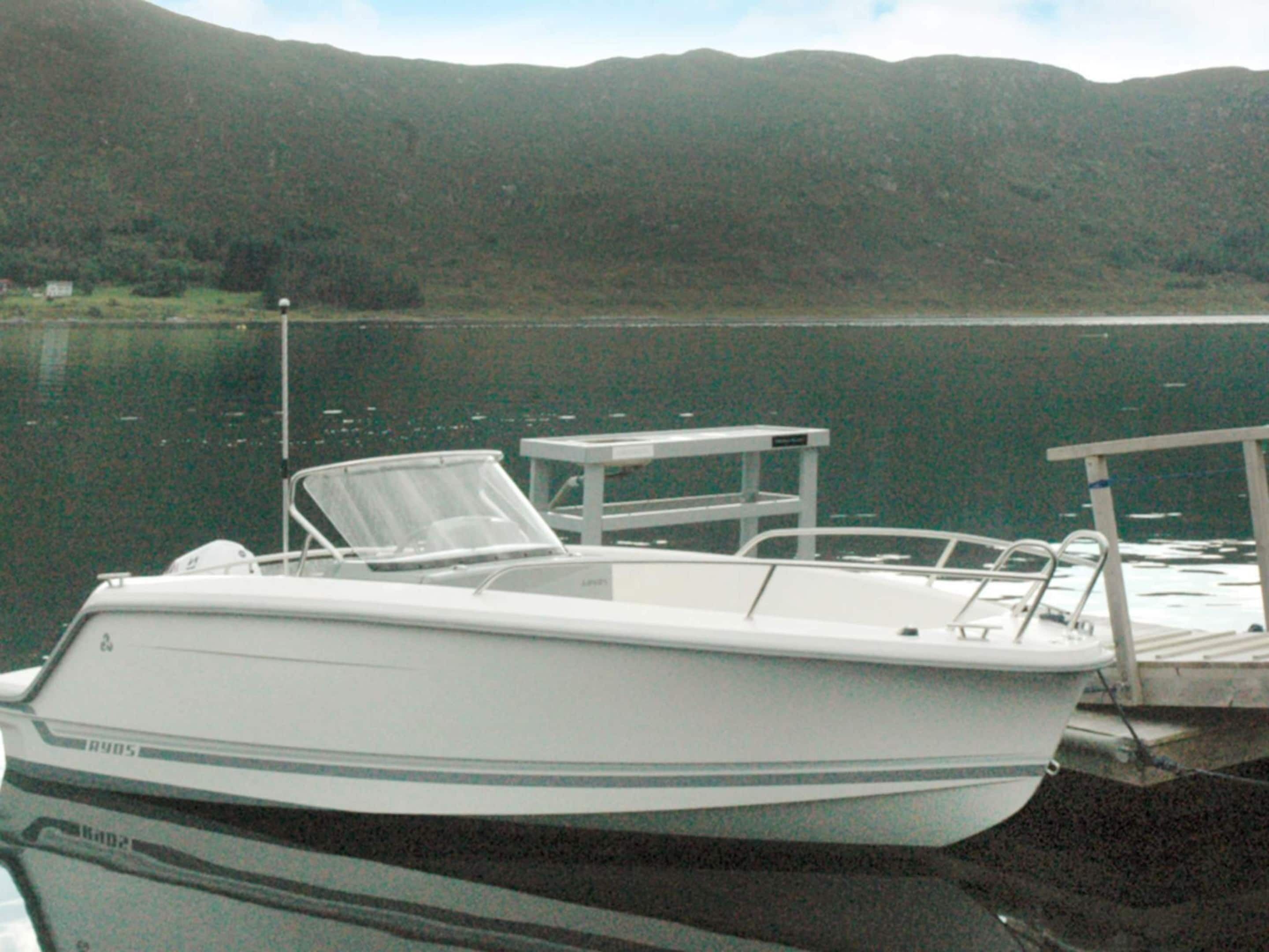 A boat docked at a pier with a view of a lake and mountains in the background.