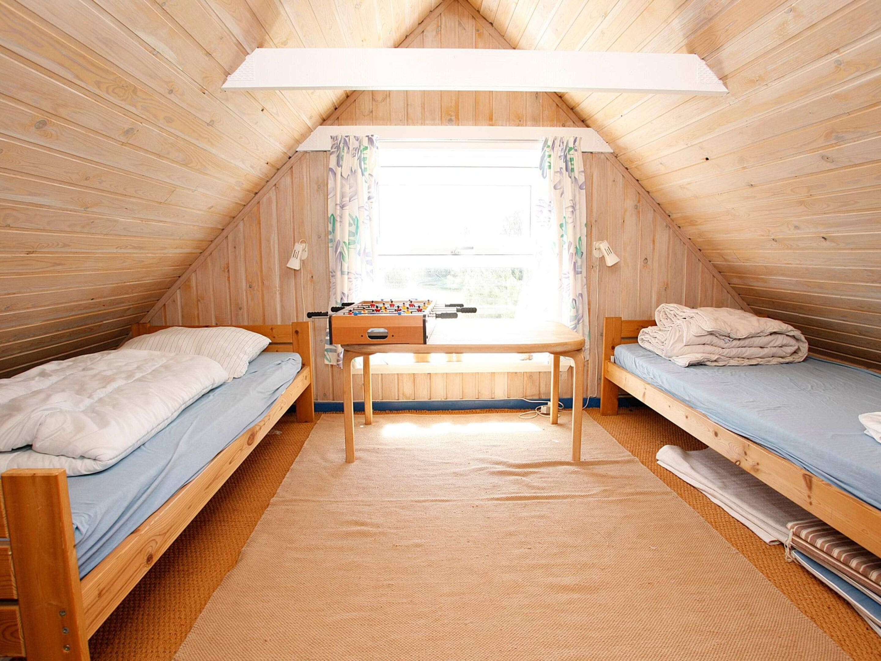 A cozy attic room with two wooden bunk beds, a small desk, and a window with curtains.