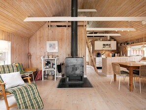A cozy cabin interior with a central fireplace, wooden walls, a dining area, and a kitchen. - 4 Star Holiday Home in Skagen (Skagen)