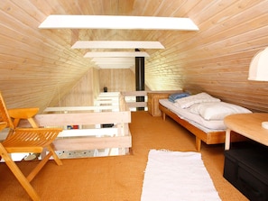 A room with a sloped ceiling, wooden walls, a bed with pillows, a chair, a small table, and a white rug. - 4 Star Holiday Home in Skagen (Skagen)