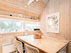 A wooden interior with a dining table, wicker chairs, a radiator, and a window with a view of trees. - 4 Star Holiday Home in Skagen (Skagen)