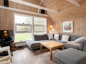 A cozy living room with a wooden ceiling, large windows, a grey sofa, a wooden coffee table, and a television. - 4 Star Holiday Home in Skagen (Skagen)