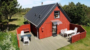 A red wooden building with a sloped roof, a deck with a table and chairs, and a covered outdoor area. - 4 Star Holiday Home in Skagen (Skagen)