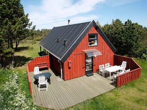 En röd träbyggnad med ett sluttande tak, en veranda med ett bord och stolar samt ett takförsett utomhusområde.
