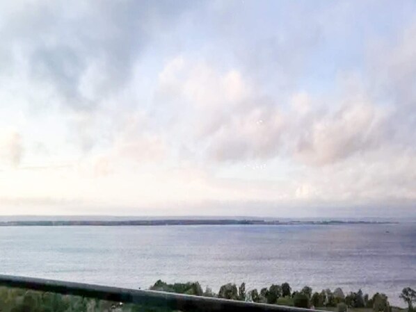 A view of a body of water with a distant shoreline and a cloudy sky.
