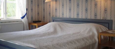 A bedroom with a bed, two bedside tables, a window with curtains, and patterned wallpaper.