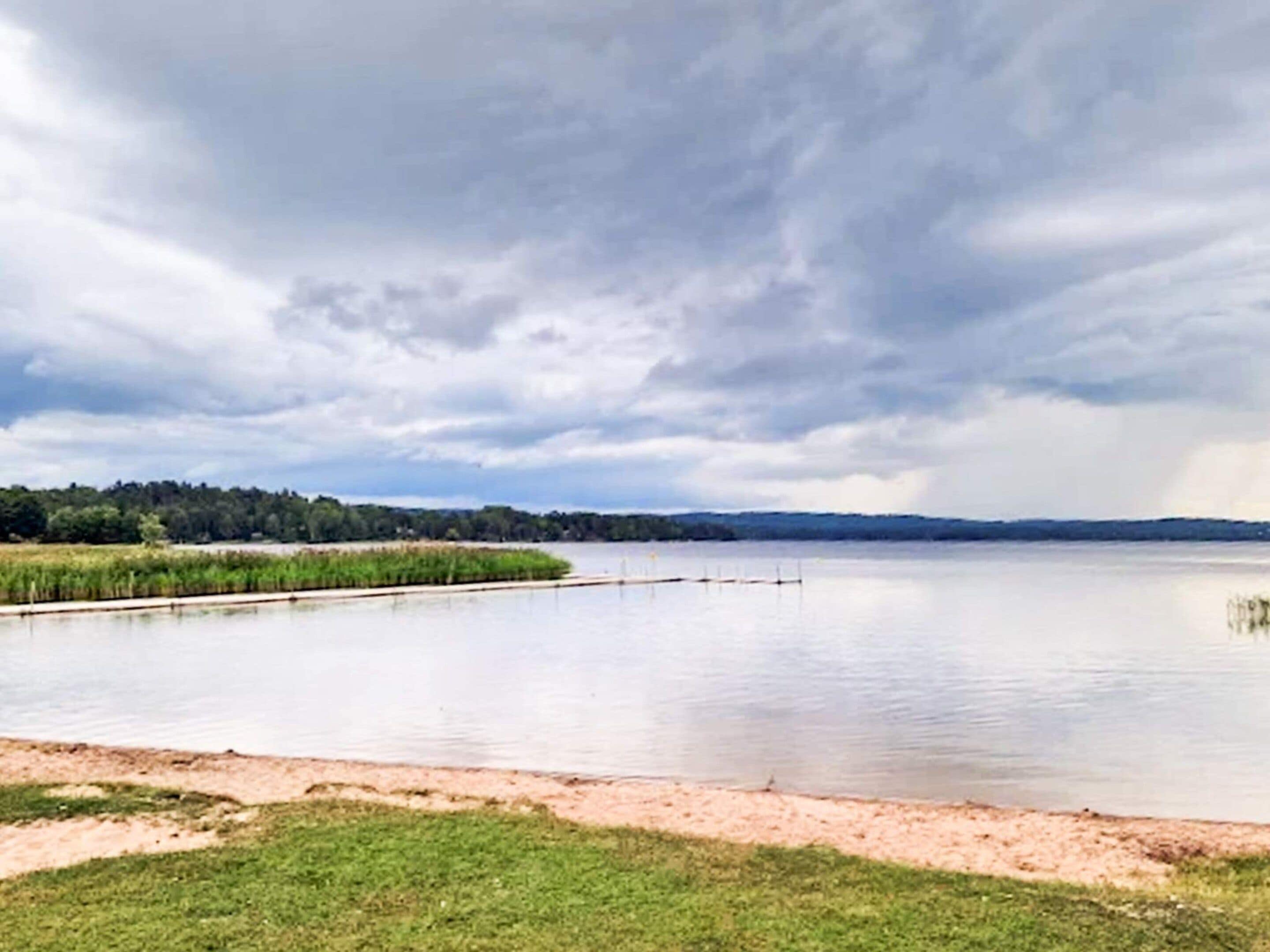 A calm lake with a grassy shore and a cloudy sky.