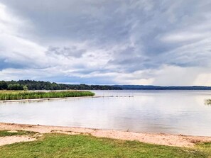 Un lac paisible, bordé d’une rive herbeuse, sous un ciel nuageux.