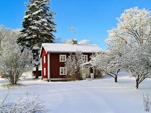 A red house with a metal roof, surrounded by snow-covered trees and a clear blue sky.