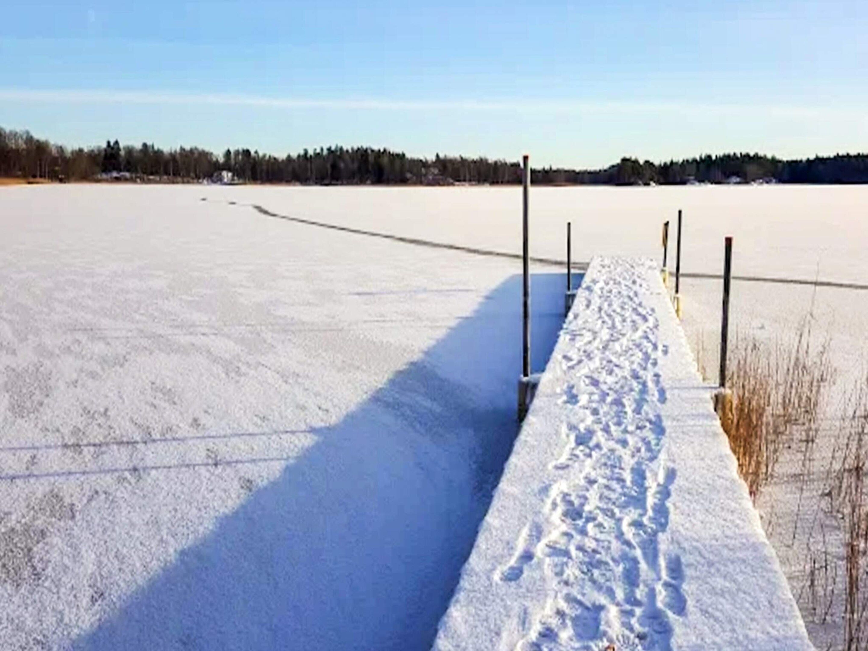 Ein mit Schnee bedecktes Feld mit einem Holenzaun und blauem Himmel.