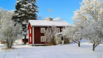 A red house with a metal roof, surrounded by snow-covered trees and a clear blue sky.