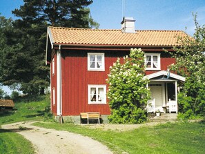 A red house with a tiled roof, a bench, and a garden.