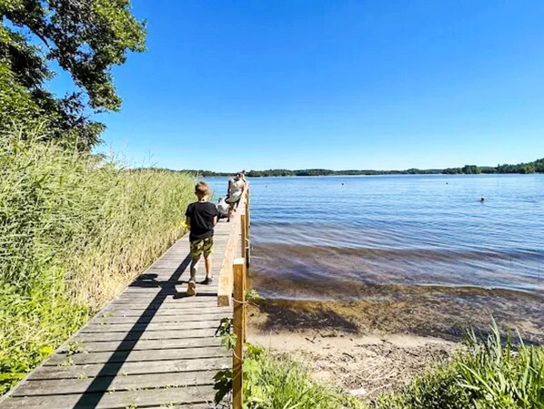 Une promenade en bois qui mène à un lac aux eaux limpides, dont la rive s’étend au loin.