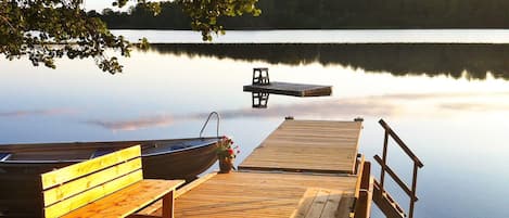 Un muelle de madera con bancos y un bote pequeño, que se adentra en aguas tranquilas.