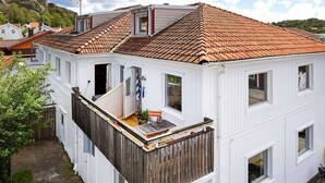 Ein weißes, zweistöckiges Haus mit roten Ziegeldach, einem Holzbalkon und einem kleinen Garten.