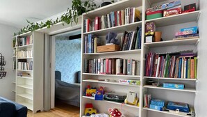 Une pièce avec une bibliothèque remplie de livres et de jouets, un berceau et un canapé bleu.