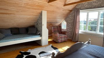 Un dormitorio estilo loft con techo inclinado, una cama, un rincón de descanso con cojines, un sillón escocés y vistas a través de una ventana.