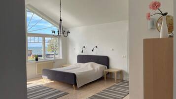 A bedroom with a bed, bedside tables, a hanging light fixture, a window with a view, and a globe on a shelf.