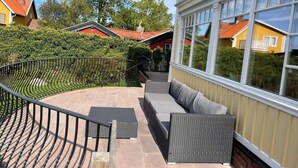 Un balcon doté d’une balustrade métallique incurvée, d’un espace salon avec des coussins gris et offrant une vue sur les maisons et les arbres des environs.