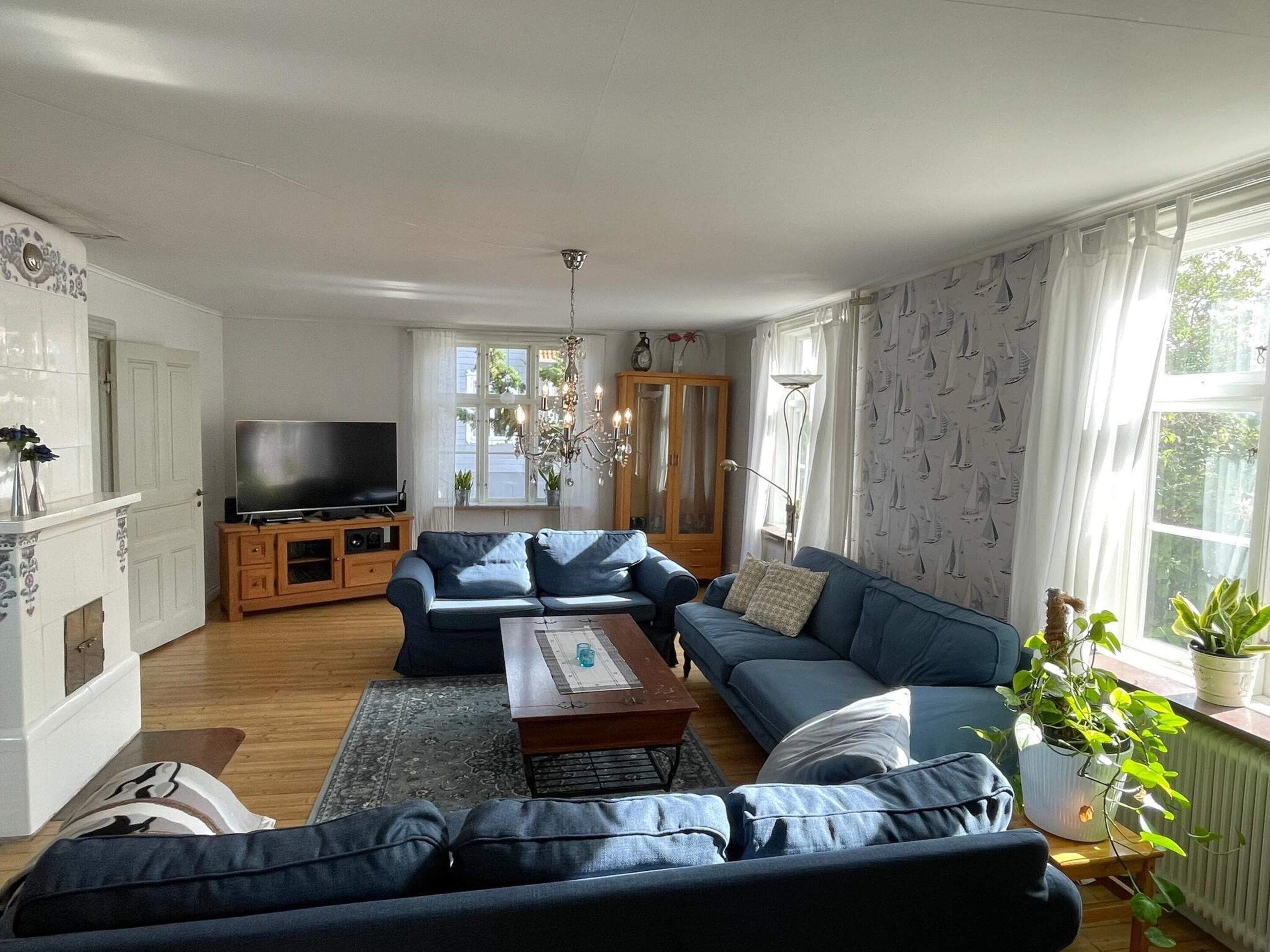 A living room with a sofa set, a coffee table, a TV on a wooden stand, and a large window with curtains.