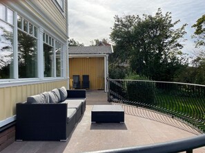 A covered patio with outdoor furniture, a stone wall, and a view of a garden.
