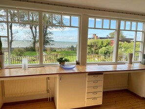 A kitchen with large windows, wooden cabinets, and a view of the sea.