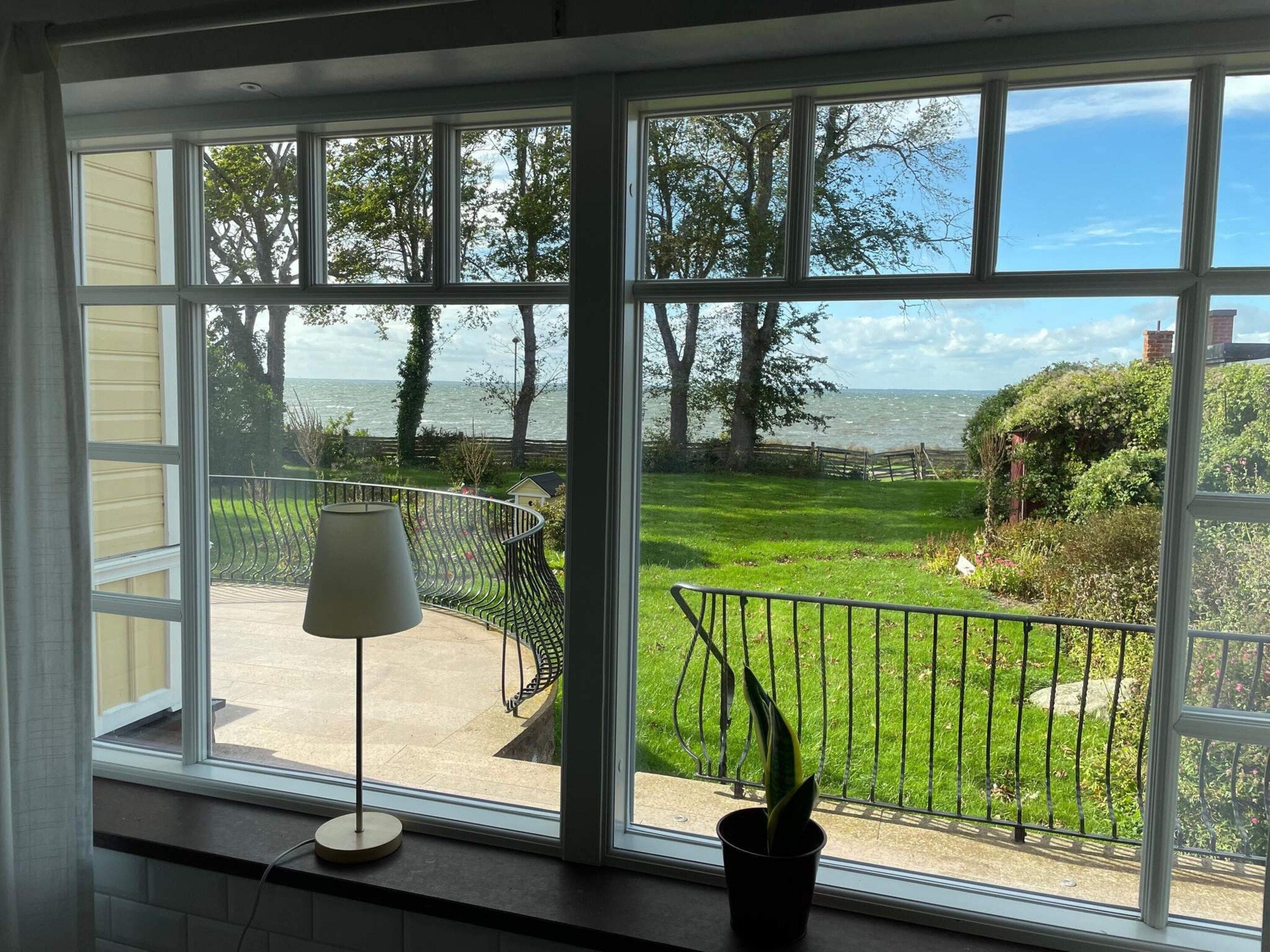 A room with large windows offering a view of a well-maintained garden and a body of water.