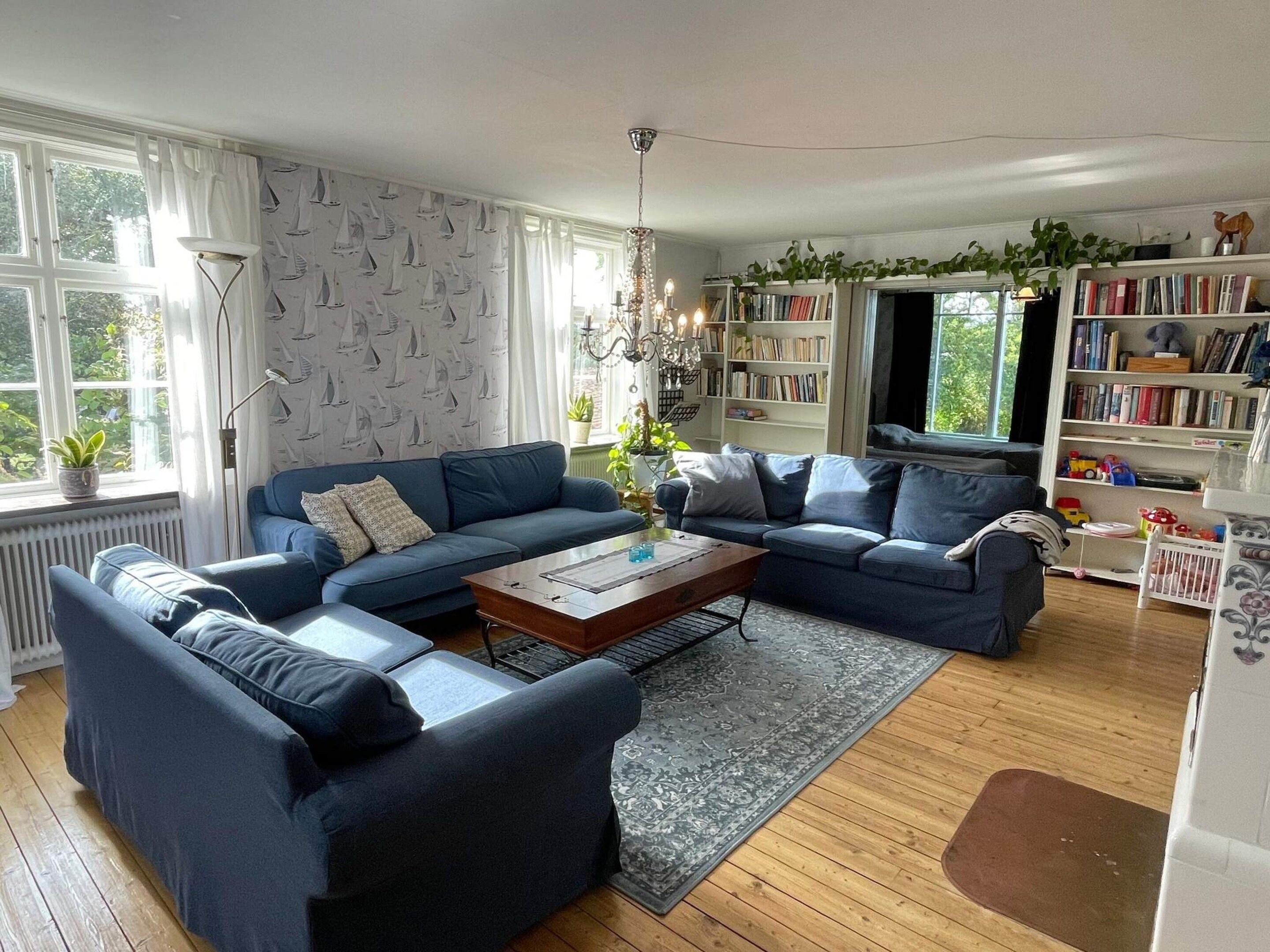A living room with a blue sofa set, a wooden coffee table, and a bookshelf filled with books.