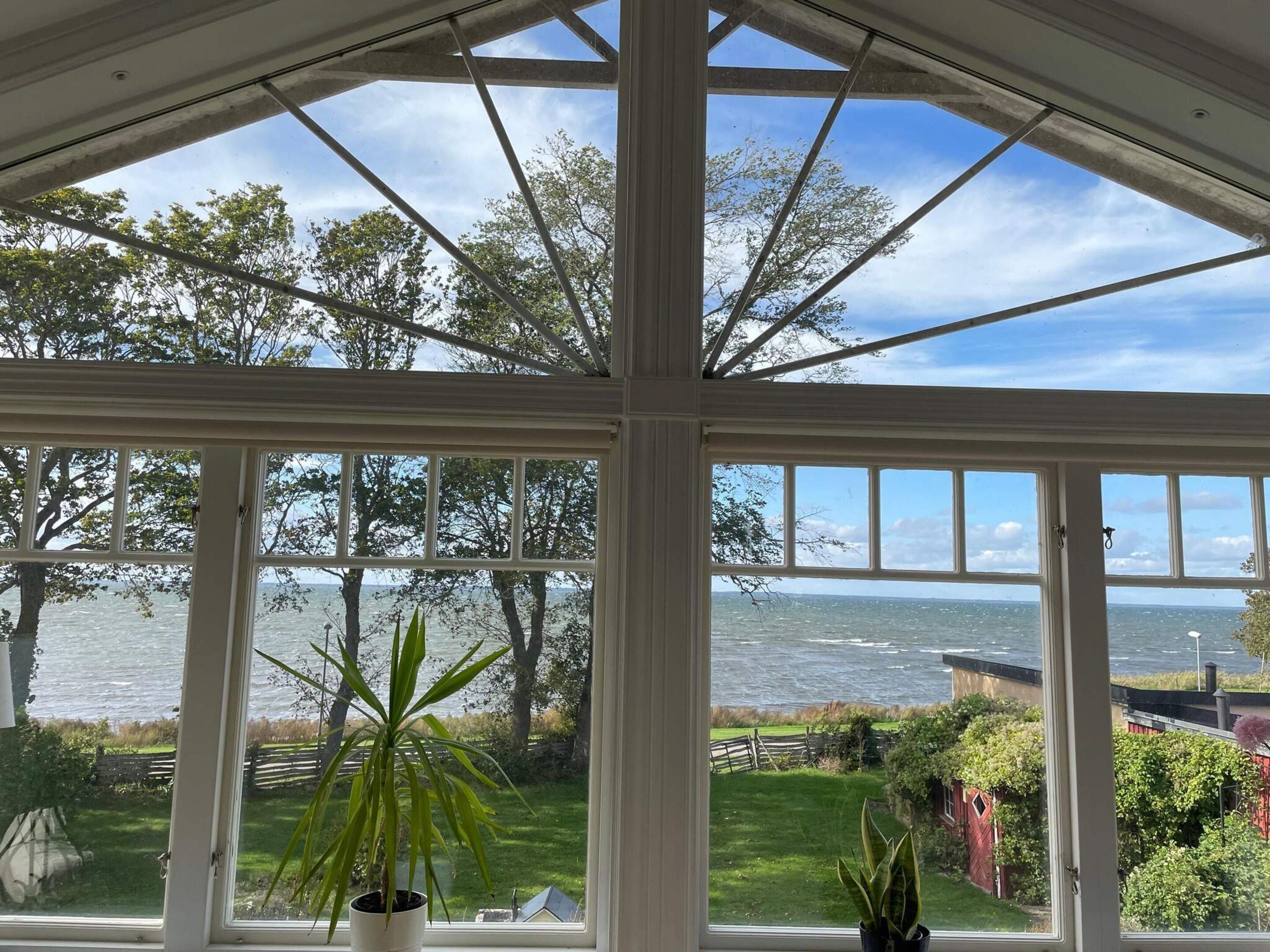 A conservatory with large windows offering a view of the sea and surrounding greenery.