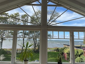 Um solário com grandes janelas que oferece vista para o mar e vegetação ao redor.