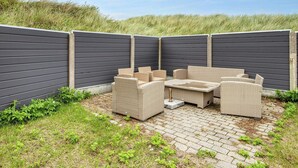 Ein Patio mit Korbmöbeln und einem Backsteinboden, umgeben von einem dunklen Zaun.