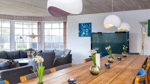 Ein moderner Arbeitsraum mit einem langen Holztisch, grauen Sofas und großen Fenstern.
